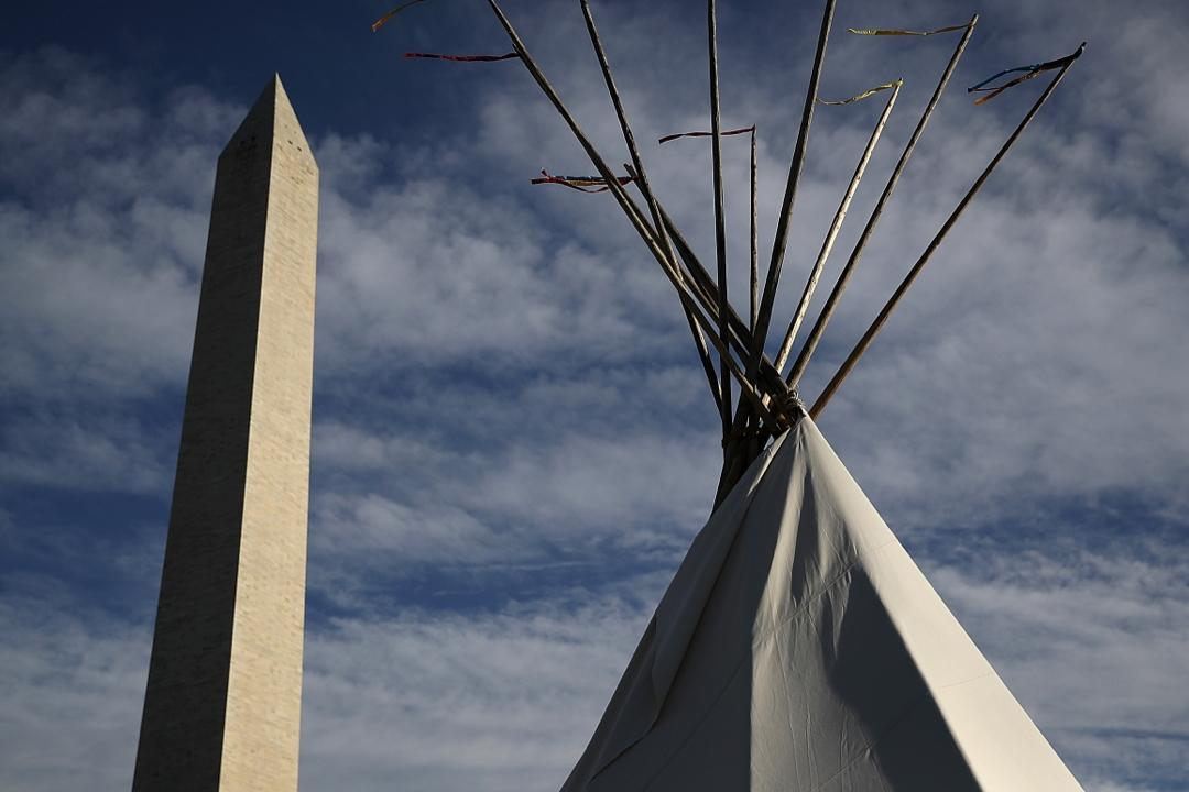 The Washington monument juts into the sky on the left side of a Native American teepee